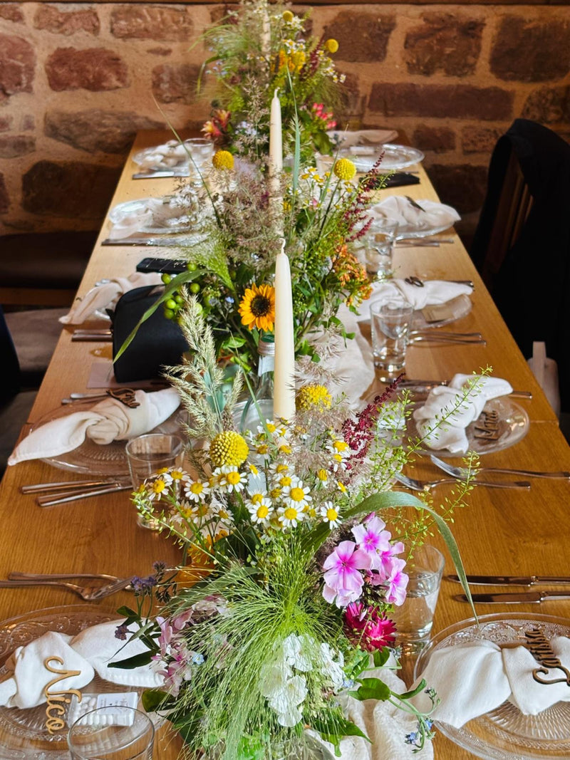 Langer Holztisch mit üppiger Wildblumen-Tischdeko in Gelb, Pink und Weiß für eine natürliche Hochzeit