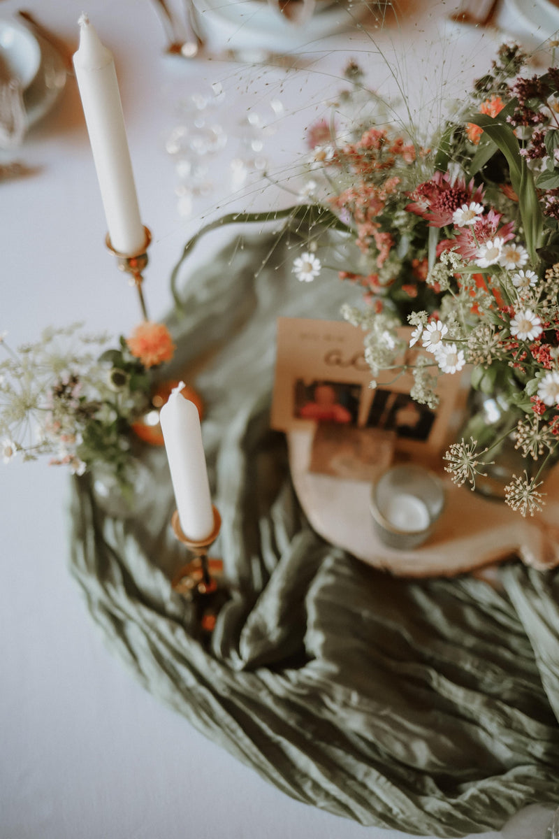 Verträumte Vintage-Tischdeko mit Wildblumen, hohem Kerzenständer und olivgrünem Tischläufer