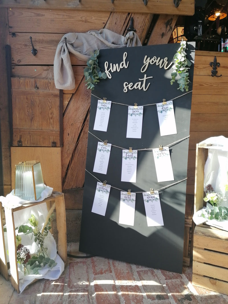 Ein Klappkarten-Plakat als Tischdeko mit der Aufschrift "find your seat" im rustikalen Bleisatz-Stil, auf dunkelblauem Hintergrund für eine Hochzeit oder Veranstaltung.